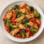 Chicken with garlic sauce, broccoli, and red bell peppers served on a white plate